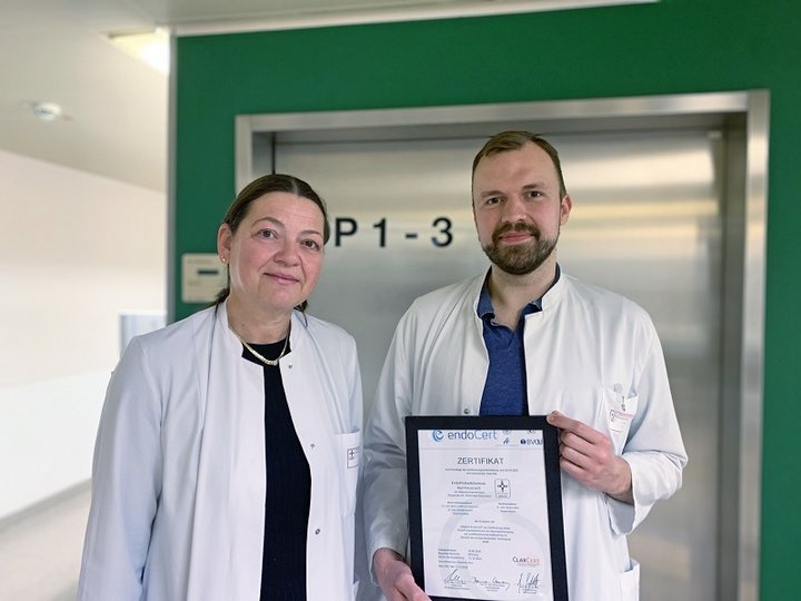 Frau und Mann in Arztkitteln halten Urkunde in der Hand