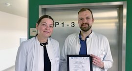 Frau und Mann in Arztkitteln halten Urkunde in der Hand