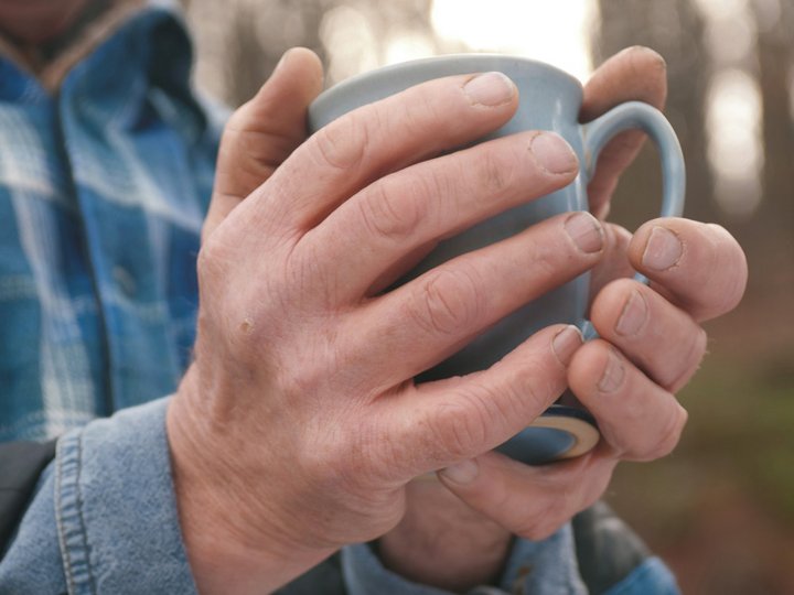 Hände eines Mannes halten einen Becher mit heißem Getränk