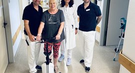 Frau auf einem Spezialroller im Krankenhaus, begleitet von Ärztin und zwei Physiotherapeuten