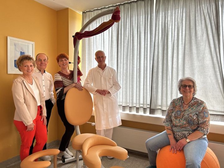 In der Mitte des Bildes steht ein Gebärstuhl. Darum stehen und sitzen mehrere Personen