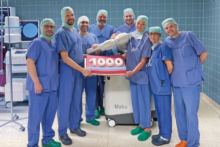 Menschen in OP-Kleidung halten Kuchen in Form einer 1000