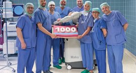 Menschen in OP-Kleidung halten Kuchen in Form einer 1000