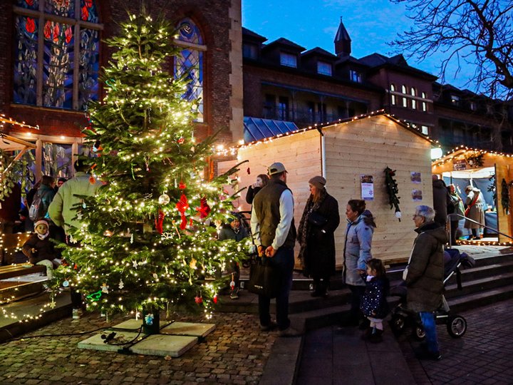Geschmückter Weihnachtsbaum, Menschen und Hütten vor der Diakonie Kirche