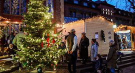 Geschmückter Weihnachtsbaum, Menschen und Hütten vor der Diakonie Kirche