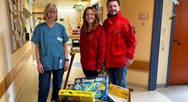 Personen lachen in die Kamera. Vor ihnen steht ein Wagen mit Spielsachen