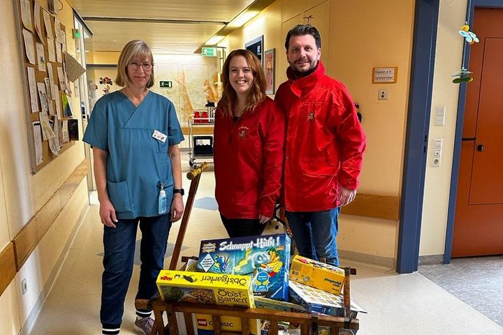 Personen lachen in die Kamera. Vor ihnen steht ein Wagen mit Spielsachen