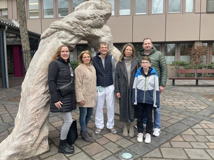 Personen stehen vor einem Krankenhaus und lächeln