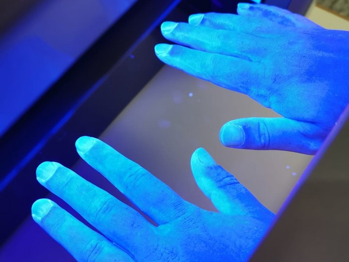Hände werden in eine Schwarzlichtlampe gehalten