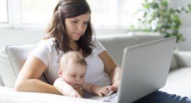 Junge Mutter mit Baby sitzt auf der Couch und chattet mit TeleHebamme