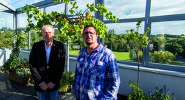 Zwei Männer lächeln auf der Dachterrasse in die Kamera