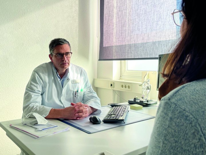 Person sitzt an einem Schreibtisch und unterhält sich mit einer anderen Person