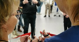 Zwei Pflegekräfte durchneiden mit der Schere ein rotes Band