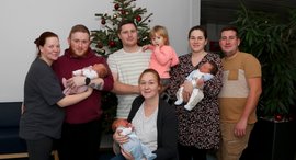 Drei Frauen und drei Männer halten drei Babys und ein Kleinkind auf den Armen