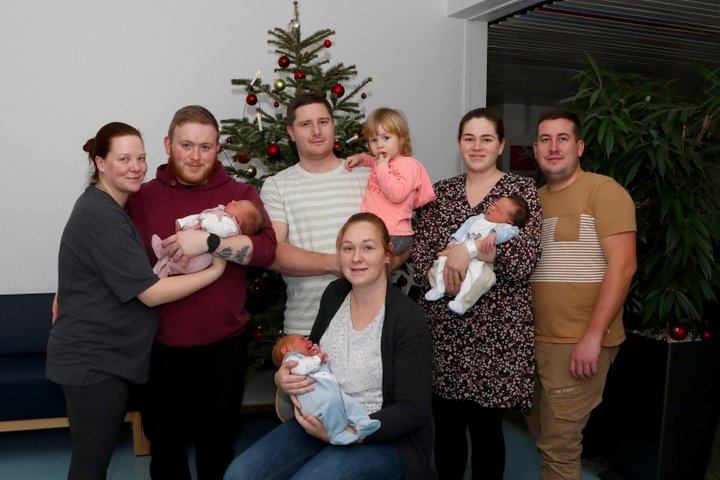 Drei Frauen und drei Männer halten drei Babys und ein Kleinkind auf den Armen