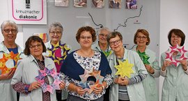 Acht Frauen in grünen Kitteln halten gebastelte Sterne in den Händen