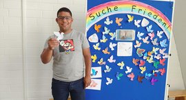 Person steht vor einer Wand mit Papiertauben und hält eine Taube in der Hand